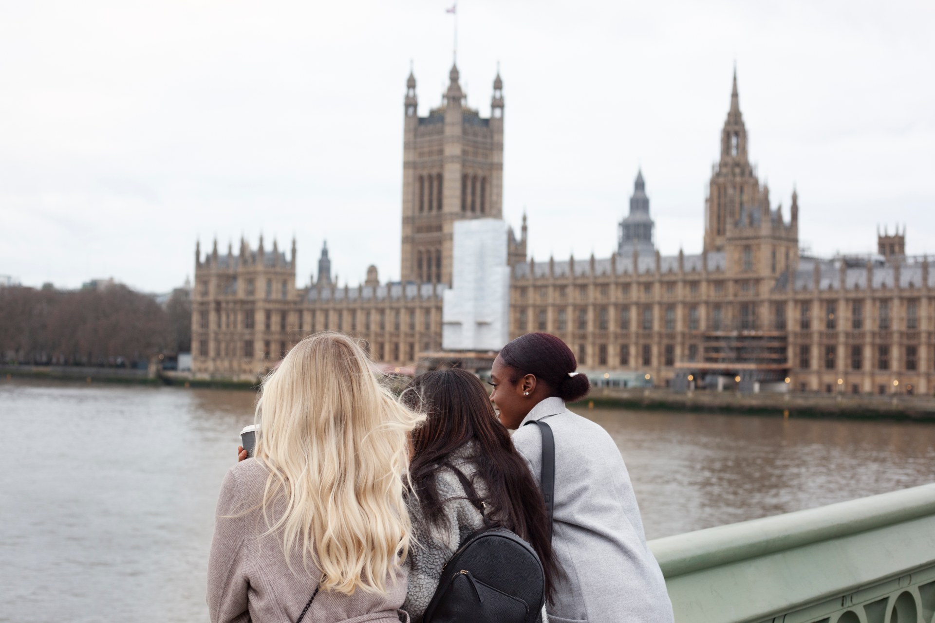 Tres jóvenes junto al Támesis en Londres, con el Palacio de Westminster al fondo